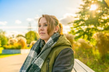 Genç bir kadın sonbaharda bir park bankında mutlu bir şekilde oturur.