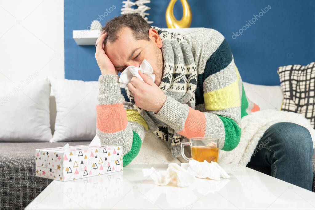 a man with flu leans ill on his table in the living room