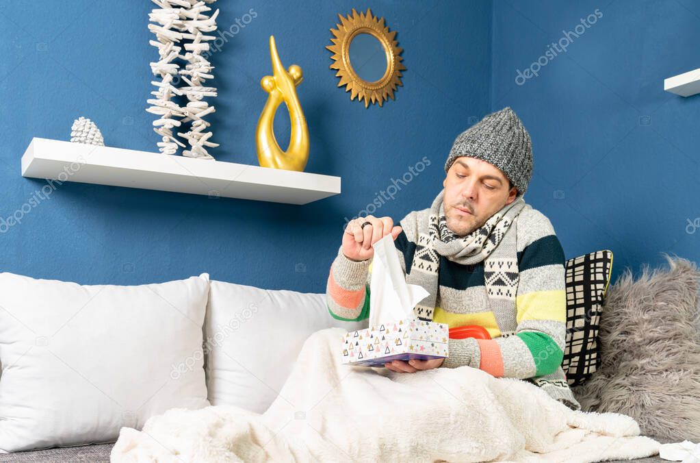 a man with flu lies on the couch and takes a handkerchief