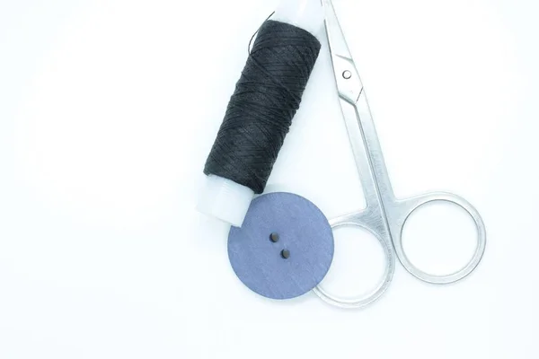Carrete de hilo negro, un botón y tijeras situado sobre un fondo blanco — Foto de Stock