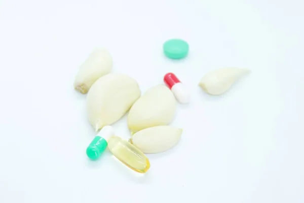 Beyaz arka planda soyulmuş sarımsak ve vitaminler var.
