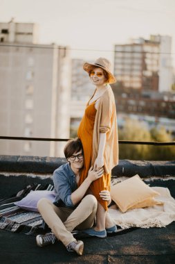happy young couple having fun  on the building rooftop. Redhead Pregnant women with her husband at sunset time