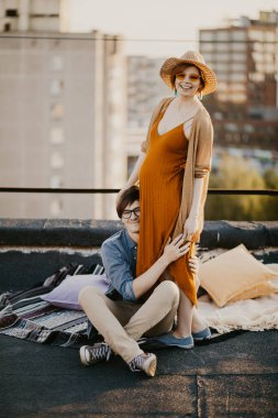 happy young couple having fun  on the building rooftop. Redhead Pregnant women with her husband at sunset time
