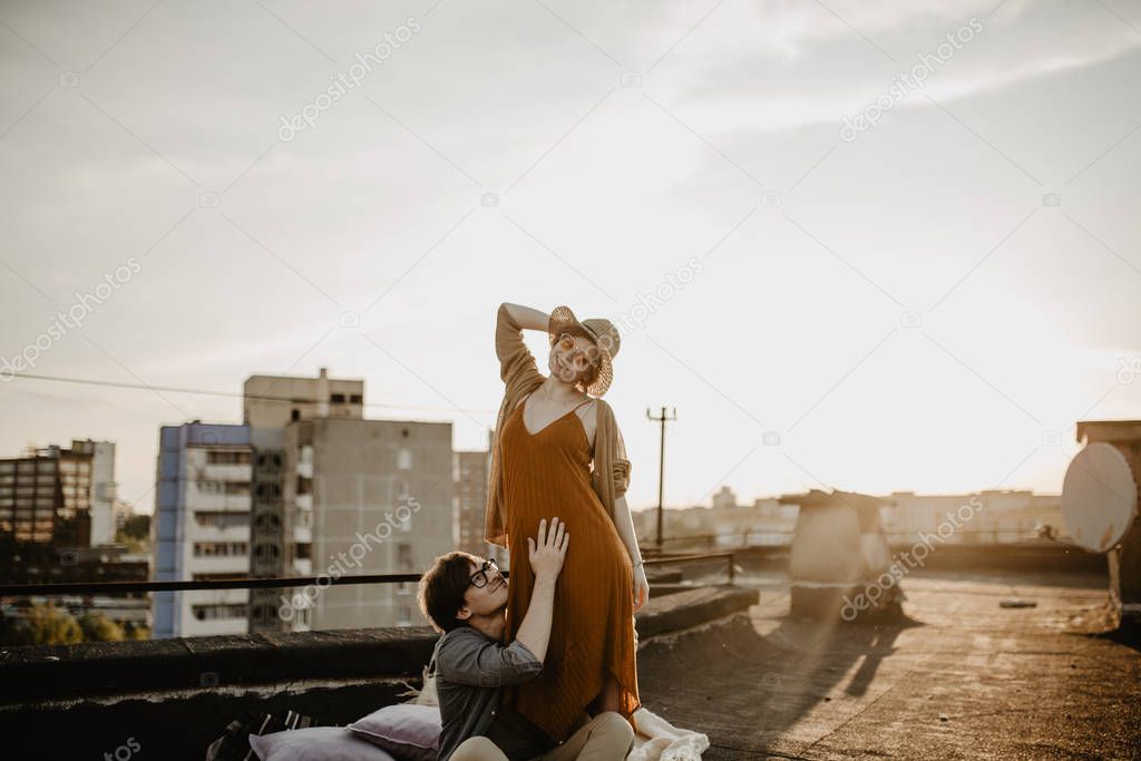 happy young couple having fun  on the building rooftop. Redhead Pregnant women with her husband at sunset time