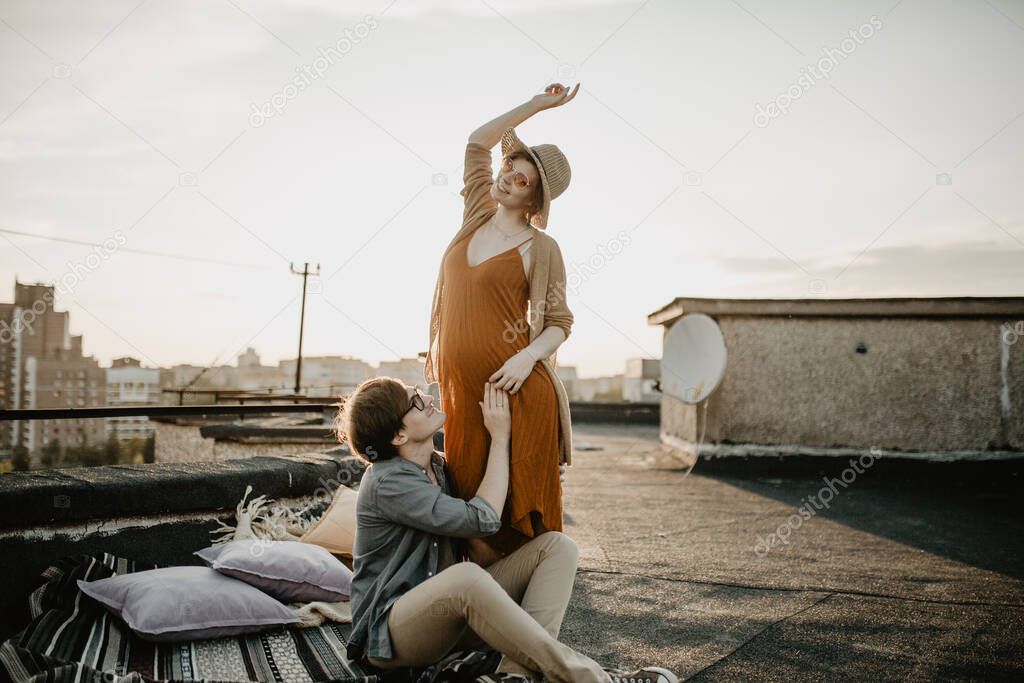 happy young couple having fun  on the building rooftop. Redhead Pregnant women with her husband at sunset time