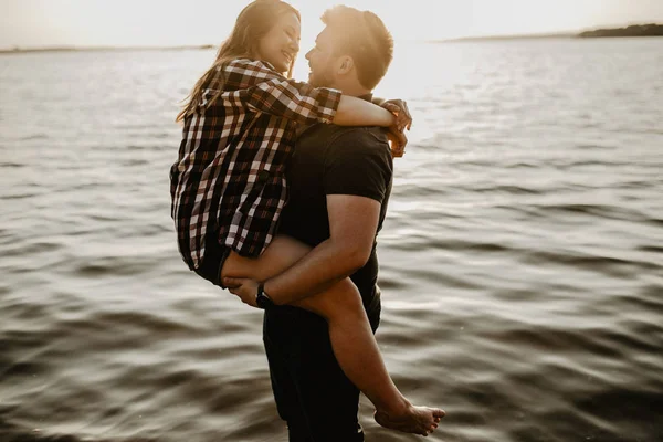 Güzel mutlu çift göl kenarında eğleniyor. Gün batımında romantik bir fotoğraf. Sarılmak ve gülümsemek.