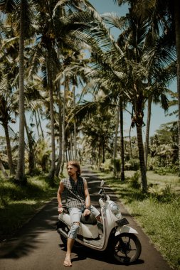 Arka planda palmiye ağaçları olan scooter 'da oturan genç adam.