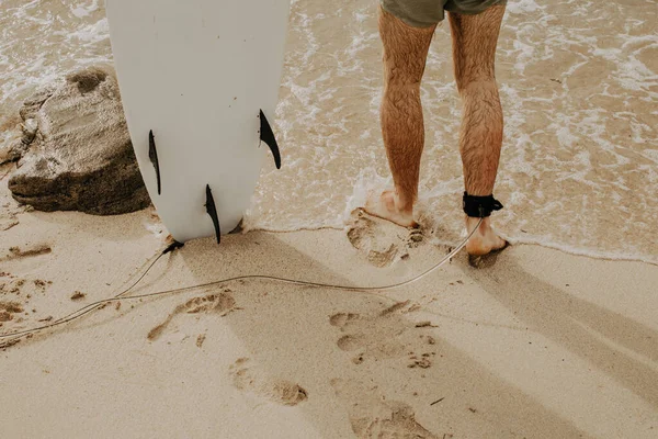 夕阳西下 冲浪手站在沙滩上的冲浪板上 俯瞰着人类的腿 — 图库照片