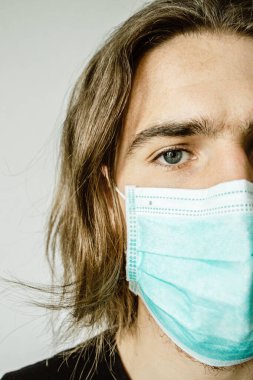 Gri arka planda yüzü tıbbi maske takan genç bir hippinin portresi. Coronavirus konsepti. 