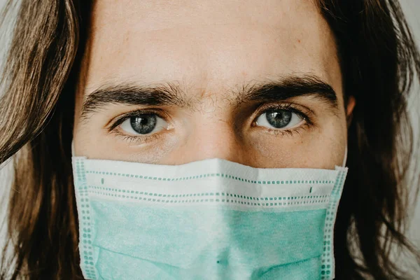 close up Portrait of a young hipster man with face medical mask on grey background. Coronavirus concept.