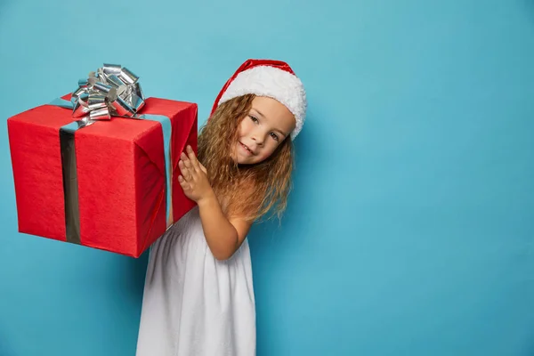 Mädchen mit Weihnachtsmann roten Hut hält Weihnachtsgeschenk — Stockfoto