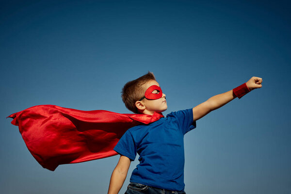 Super hero child (boy) against blue sky