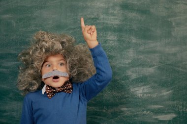 Yeşil karatahtaya karşı neşeli gülümseyen küçük çocuk. Kameraya bakıyorum. Biraz Einstein tarzı. Okul kavramı