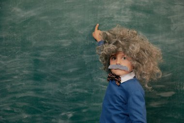 Yeşil karatahtaya karşı neşeli gülümseyen küçük çocuk. Kameraya bakıyorum. Biraz Einstein tarzı. Okul kavramı