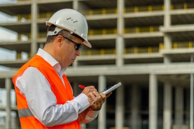 İnşaat mühendisi gömlekli ve kravatlı güvenlik kaskı ve yeleği olan adam inşaat alanında çalışıyor. Endüstriyel alanda çalışan insanlar kavramı