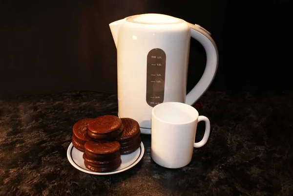 Electric kettle, cup and chocolate chip cookies.