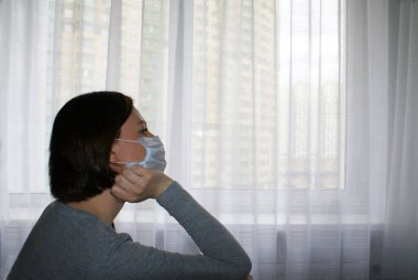 Karantina altındaki tıbbi maskeli kız pencerenin yanındaki evde.