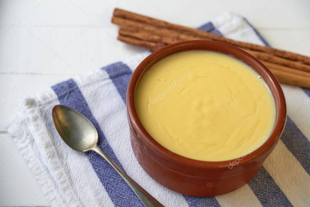 Catalan cream served in a clay bowl with a silver spoon, on top of a blue and white napkin, on a rustic white wooden table.