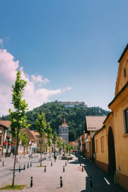 Rasnov, Romanya - 1 Ağustos 2017: Antik Sakson kasabasının ana caddesi güneşli bir günde. Tepedeki güçlendirilmiş kilise ve ortaçağ şatosu.