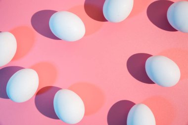 Beyaz tavuk yumurtaları mutfak masasının üstünde. Boş alan, mesaj için yer. Yaratıcı minimalist stil soyut Paskalya konsepti. Moda sert hafif düz arkaplan üzerinde uzanan pastel pembe arkaplan.