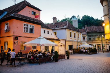Brasov, Romanya - 1 Ağustos 2017: İnsanlar yaz akşamları merkez konsey meydanı (Piata Sfatului) yakınlarındaki eski kentin kafesinde eğleniyorlar. Şehir mavi saat yaşam sahnesi.