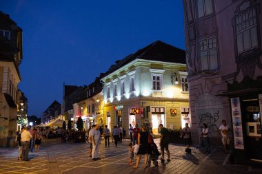 Brasov, Romanya - 1 Ağustos 2017: İnsanlar yaz akşamları sokaklarda yürüyor. Şehir mavi saat yaşam sahnesi.