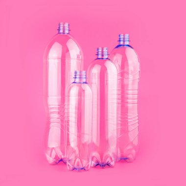 Pastel pembe arka planda kapağı olmayan dört farklı kullanılmamış boş su şişesi..