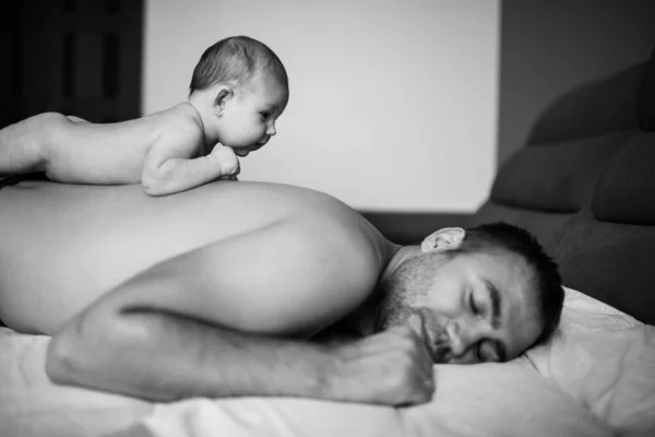 Little baby girl traveling the back of her father while he is asleep. Cute black and white family portrait. Dad and daughter relationships concept.