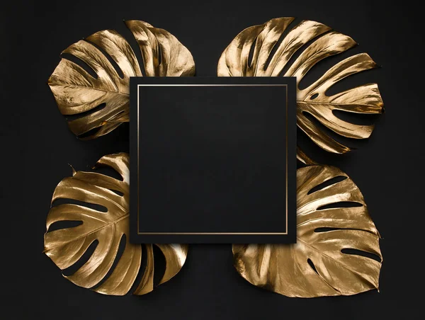 Natural monstera leaves spray painted with golden metallic paint on dark deep black background. Trendy layout border frame wtih blank card as coopy space. Creative luxury cover, invitaion template.