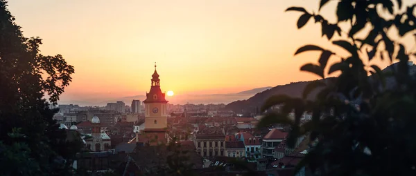 Town council hall tower morning sunrise scenic backlit view, location Brasov city, Transylvania, Romania. Famous travel destination scenic summer colorful panoramic skyline postcard.