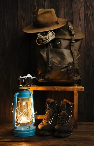 Atmospheric hiking survival vintage accessories including packed backpack, gas lamp, oldschool boots in the evening inside of remote cabin. Dark background copyspace. Wanderlust lifestyle concept.