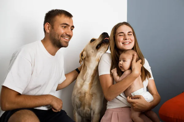 Happy family with little baby and big dog spend time together at home. Cheerful parents smiling.