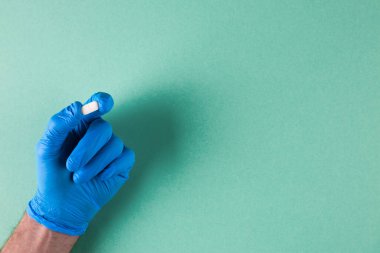 Plastik steril eldivenli eczacı elinde beyaz hapla arka planda bekliyor. Boşluk. Asgari ilaç konsepti.