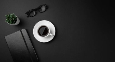Beyaz kahve fincanı, siyah deri defter, gözlük, masanın üstünde sulu bitki. Mesaj için yer var. Asgari işletme konsepti.