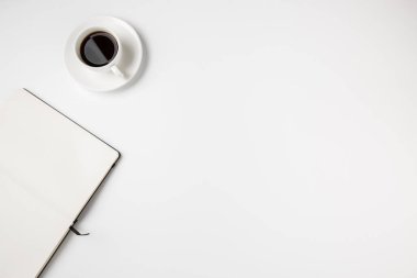 Kahve fincanı ve boş bir defter sayfası olan küçük, beyaz bir masa. Metin için yer.
