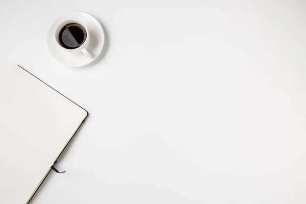 Abstract minimal white desk top with coffee cup and empty open notebook page. Room for text.