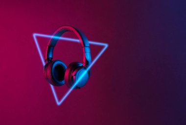 Modern siyah kablosuz kulaklıklar soyut siyah arka planda renkli ışık yayıyor. Mesaj için yer var. Neon üçgen şekli. Gelecekçi müzik konsepti.
