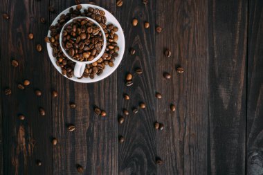 Beyaz espresso fincanındaki kahve çekirdekleri kırsal ahşap masada. Geleneksel düz konsept. Boşluğu kopyala.