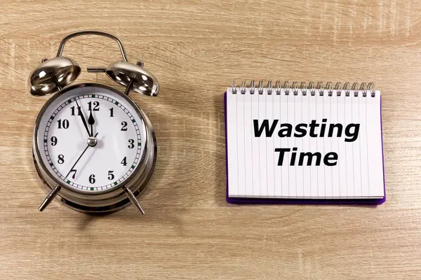 Wasting Time Concept with traditional alarm clock and a note which reads \'Wasting Time\'