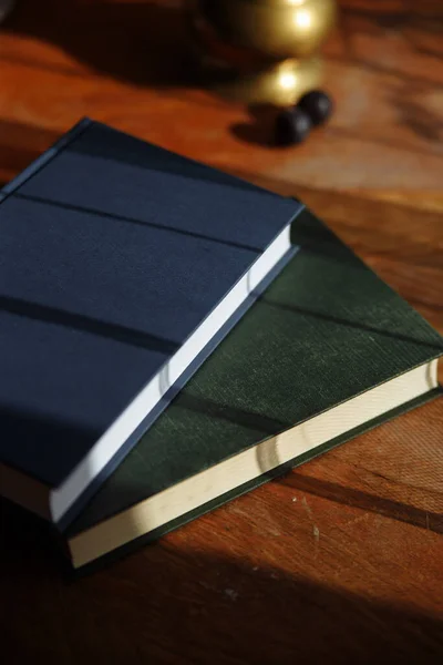 two books green and blue on a wooden table and a shadow from the curtains