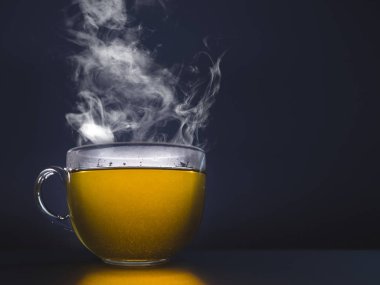 Bardakta sıcak çay. Karanlık bir arka planda buhar.
