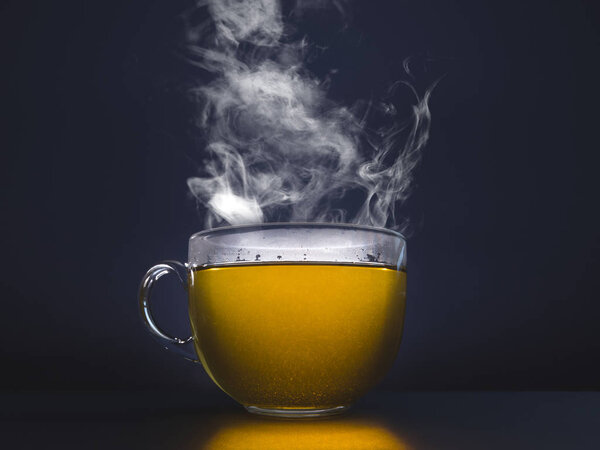 Glass cup with hot tea. Steam on a dark background.