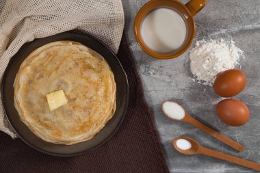 Cooking pancakes for holiday breakfast. A stack of pancakes on the table for Maslenitsa. Recipe with ingredients.