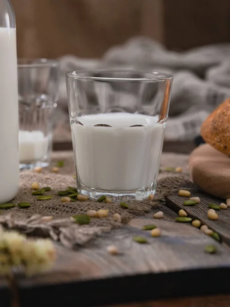 Bicchiere di latte per colazione nella Giornata Mondiale del Latte. Semi sparsi e noci su un vecchio tavolo vintage. Colpo verticale . Immagine Stock