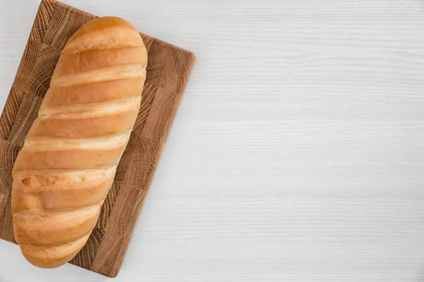 Whole loaf of bread on wooden board on white background.