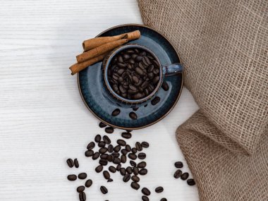 Kahve çekirdekli fincan ve beyaz masanın üzerinde bez.