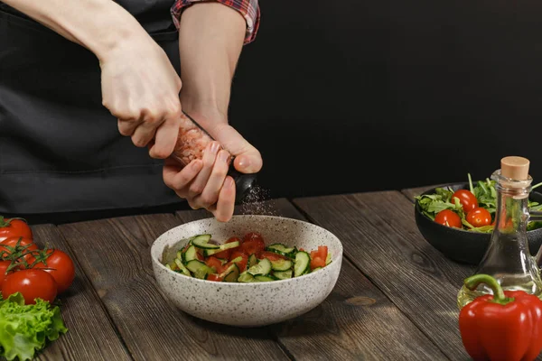 Женщина солит свежий овощной салат на деревянном столе. Женские руки с копирайтом . — стоковое фото