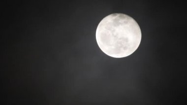 Karanlık bulutlu bir gecede dolunay. Ay 'ın önünden bulutlar geçiyor, gerçek zamanlı çekim. Geceleri bulutlar geçiyor. Geceleyin dolunay ve gerçek zamanlı bulutlar..
