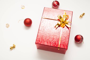 Hediye kutusu kırmızı, altın bir yay ile parlak, altın kurdeleler ve Noel toplarıyla süslenmiş, beyaz arka planda, yazıtlar için bir yer var. Yeni yıl ya da Noel için hediye kavramı.