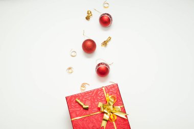 Hediye kutusu kırmızı, altın bir yay ile parlak, altın kurdeleler ve Noel toplarıyla süslenmiş, beyaz arka planda, yazıtlar için bir yer var. Yeni yıl ya da Noel için hediye kavramı.